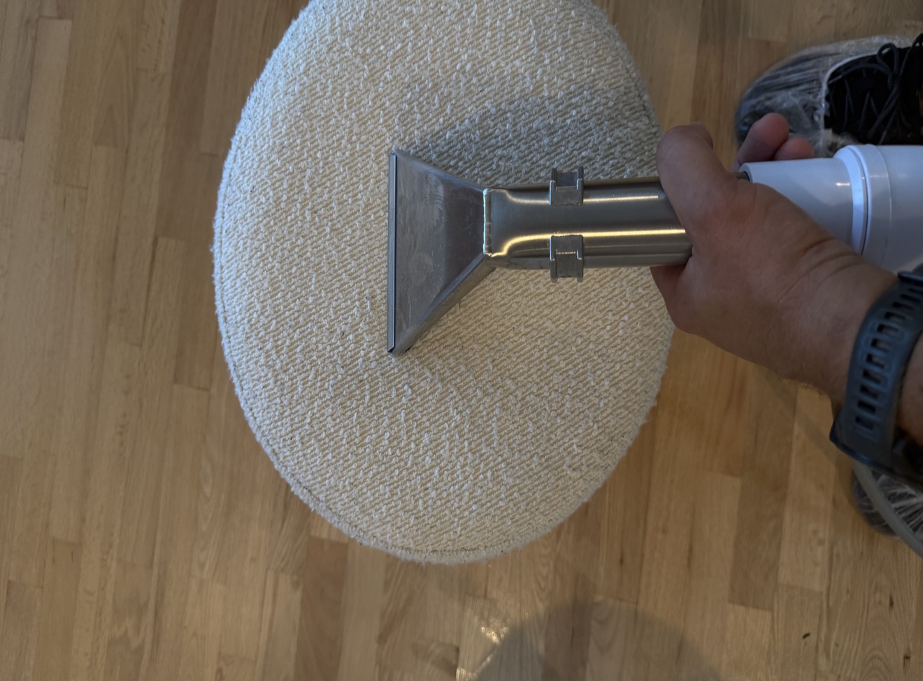 Upholstery extraction wand working across the surface of a white round ottoman during professional cleaning in Kelowna