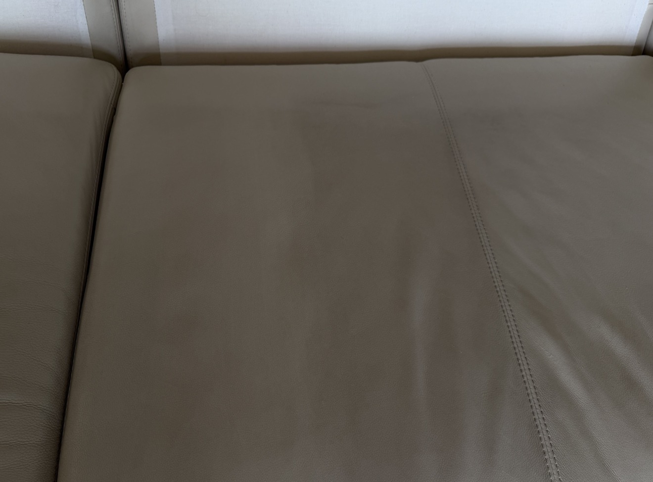 Close-up of white leather sofa seat prior to cleaning, showing surface dullness and soiling from regular use